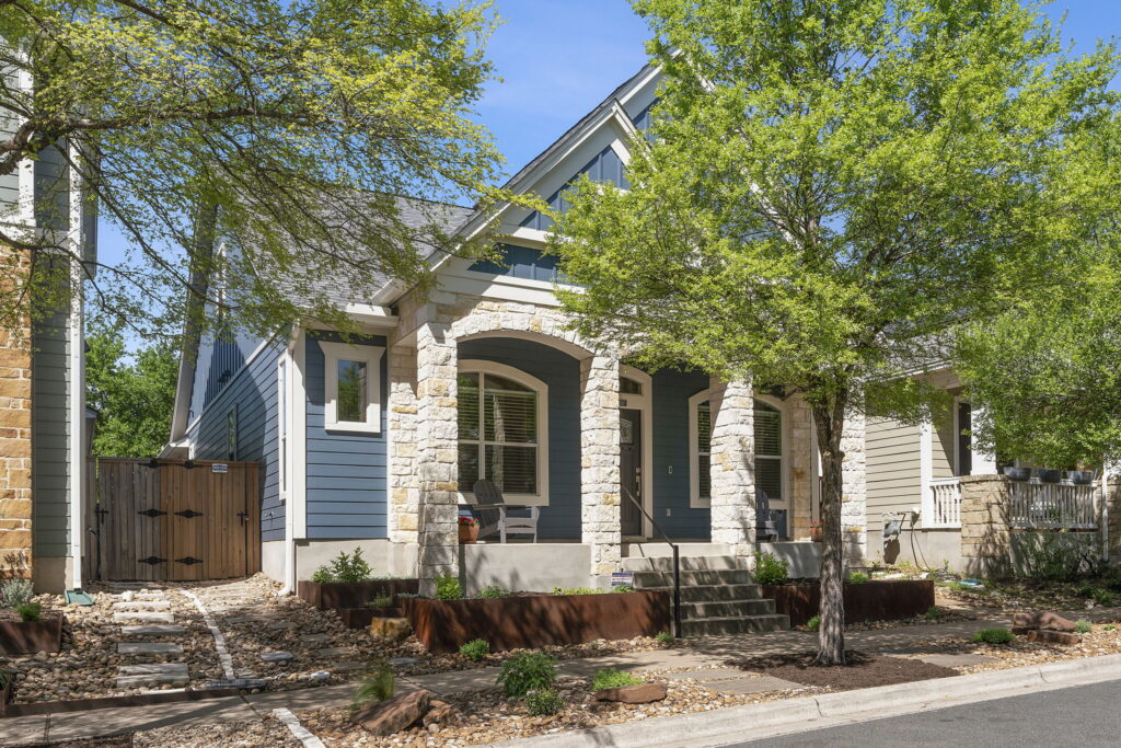 Blue craftsman style home with tree in front and stone accents.